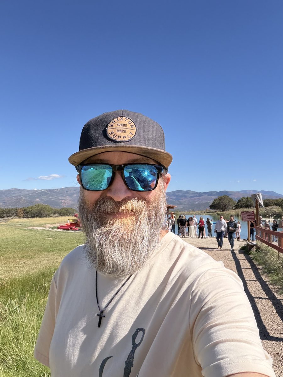 Michael taking a selfie on a lakeside path in Utah, wearing a cross necklace and sunglasses