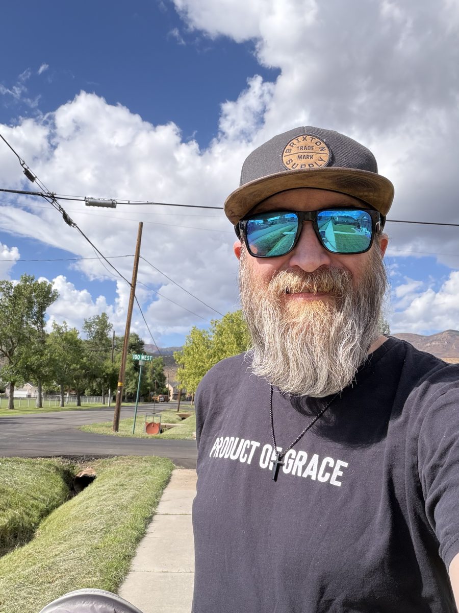Michael taking a selfie on a sunny Utah street in a black "Product of Grace" shirt and sunglasses